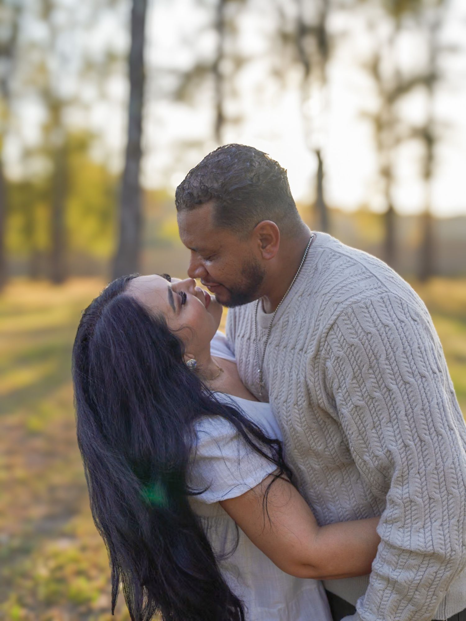 Couple sharing a romantic kiss outdoors in a sunlit forest setting, with the woman leaning back joyfully.