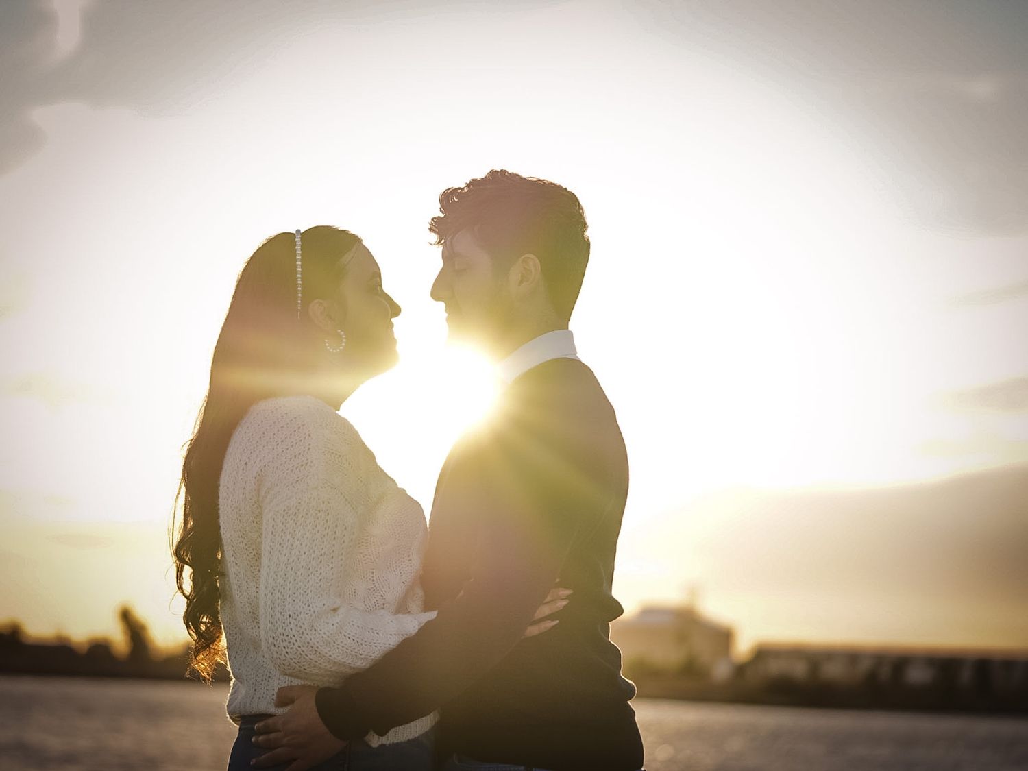 Romantic couple embracing at sunset with golden lens flare, silhouetted against a glowing sky.