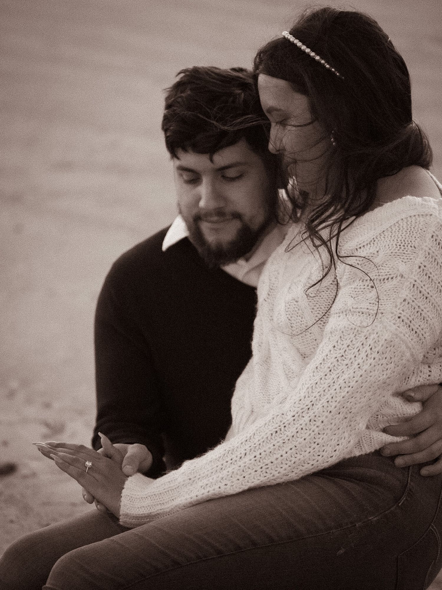 Sepia toned photo of couple sitting closely together on beach, man embracing woman tenderly.