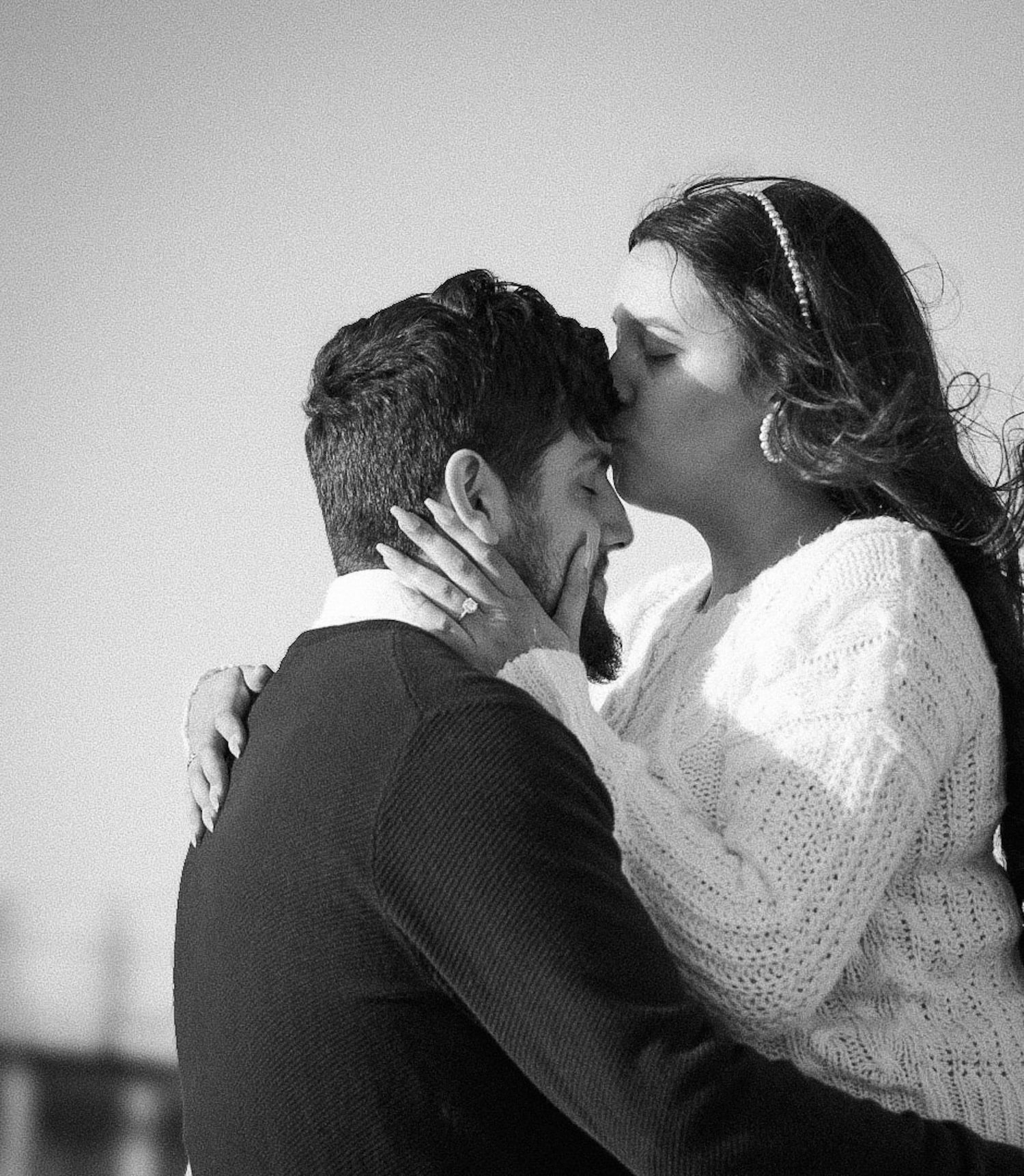 Black and white photo of a couple sharing a romantic kiss outdoors.