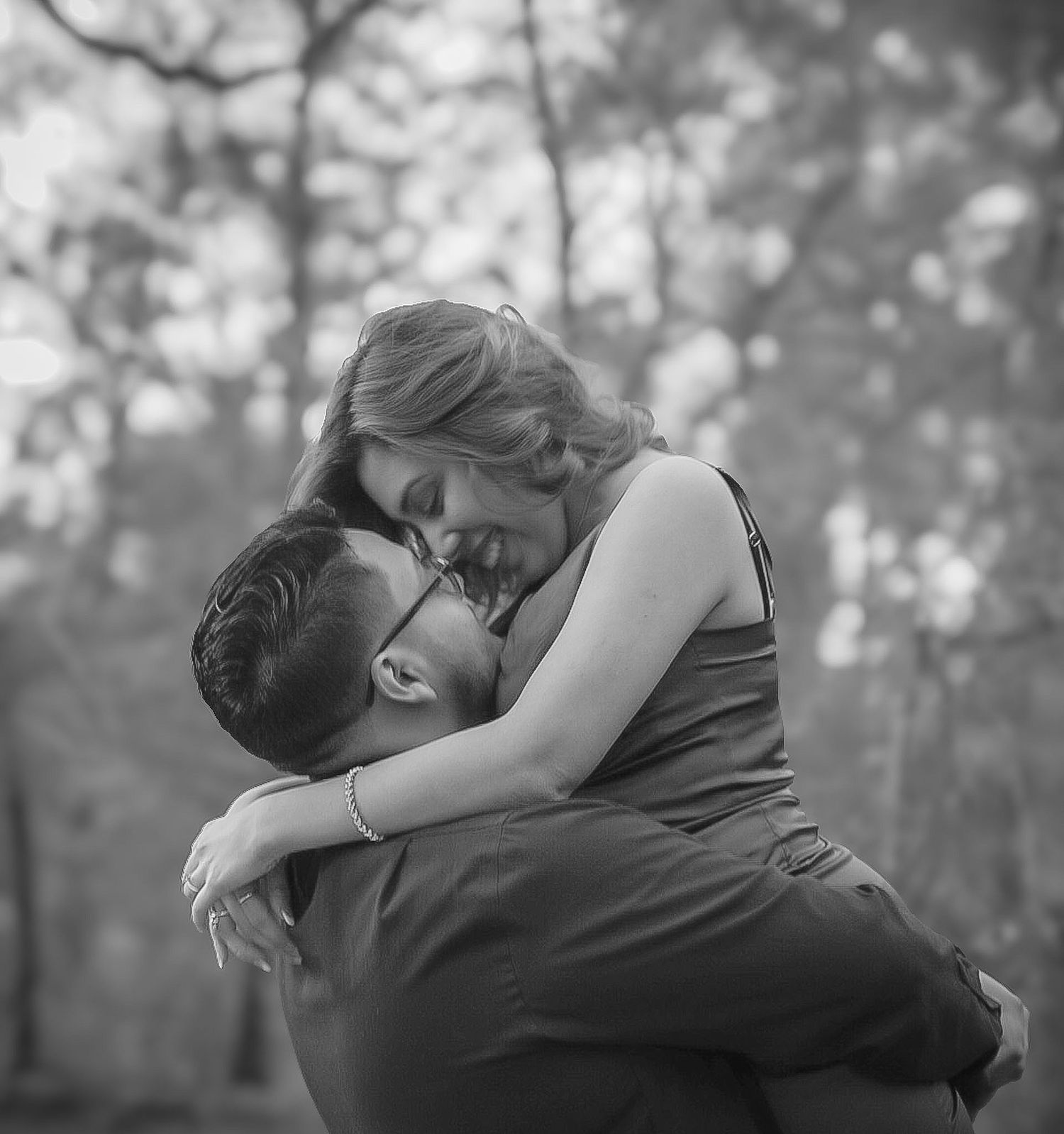 Black and white photo of a man lifting a woman in a loving embrace in the woods.