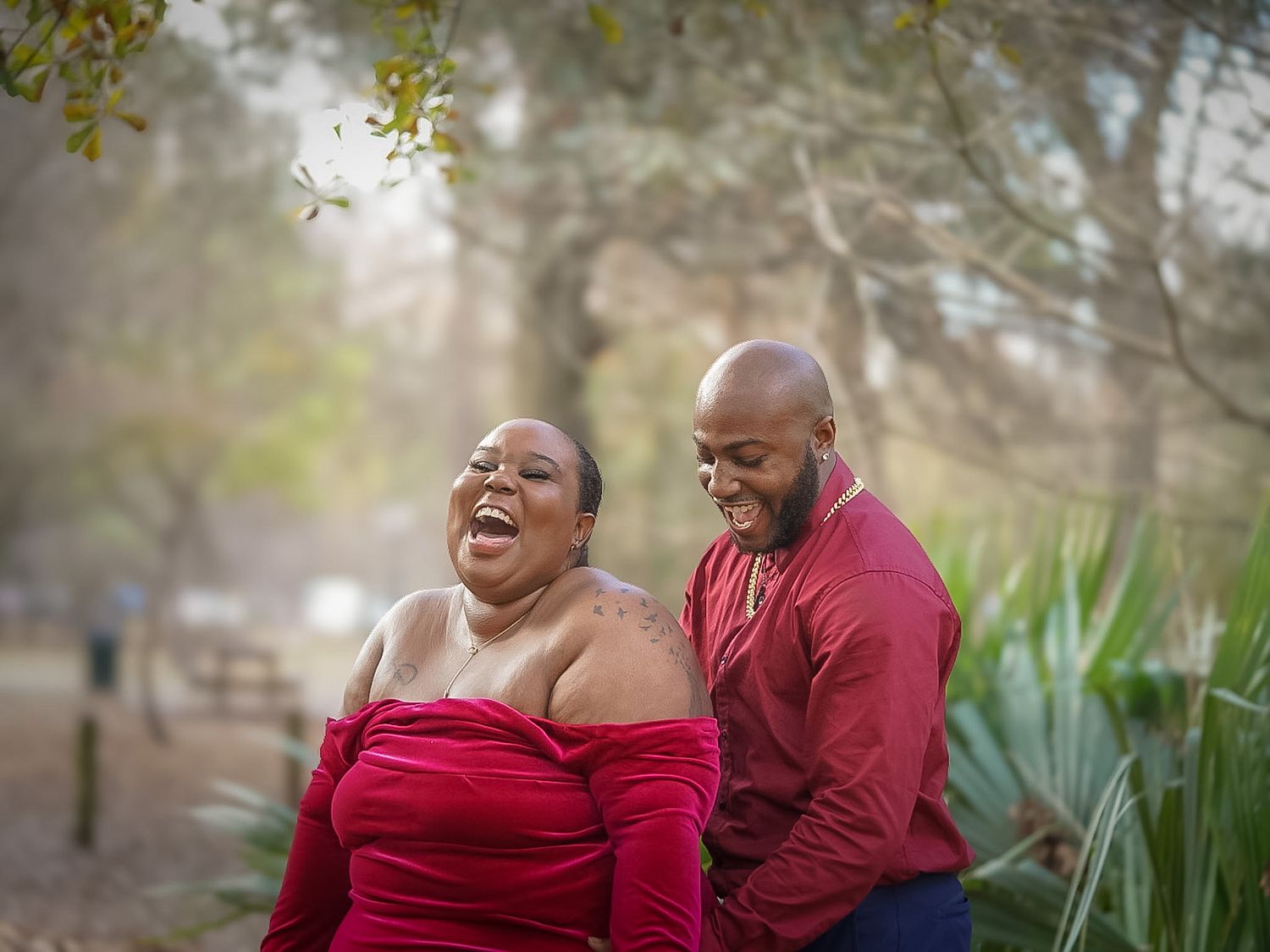 A joyful couple laughing together outdoors, wearing matching red outfits in a lush park setting.