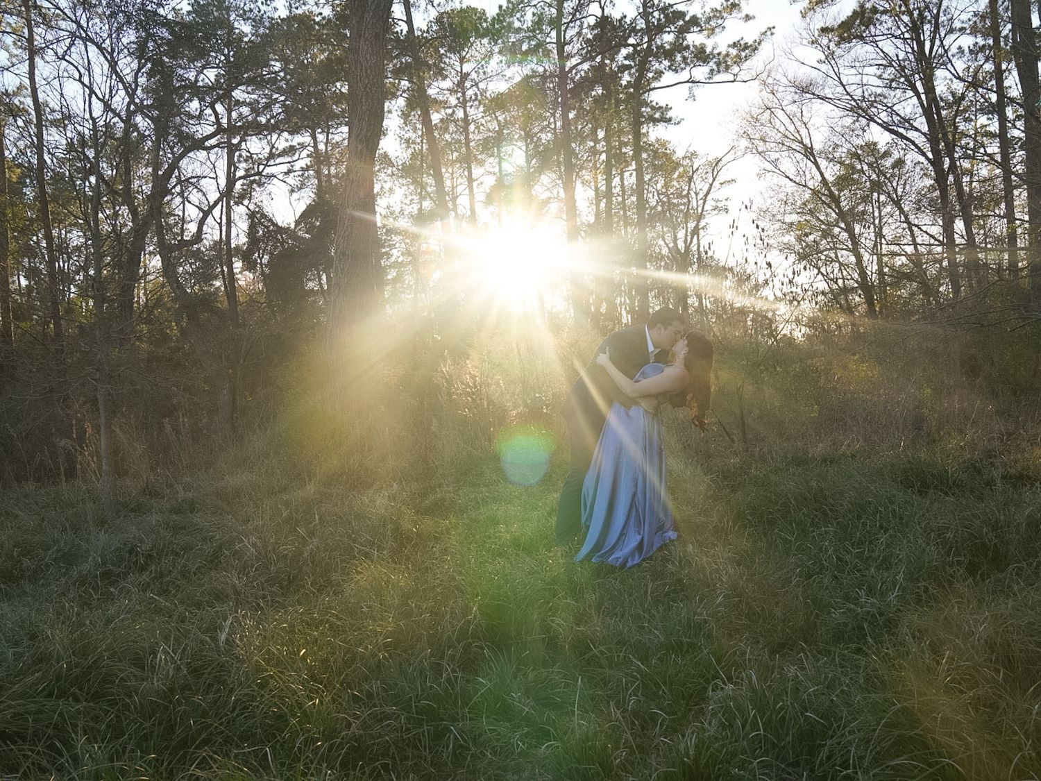 A woman in a blue dress stands in a sunlit forest clearing at golden hour.