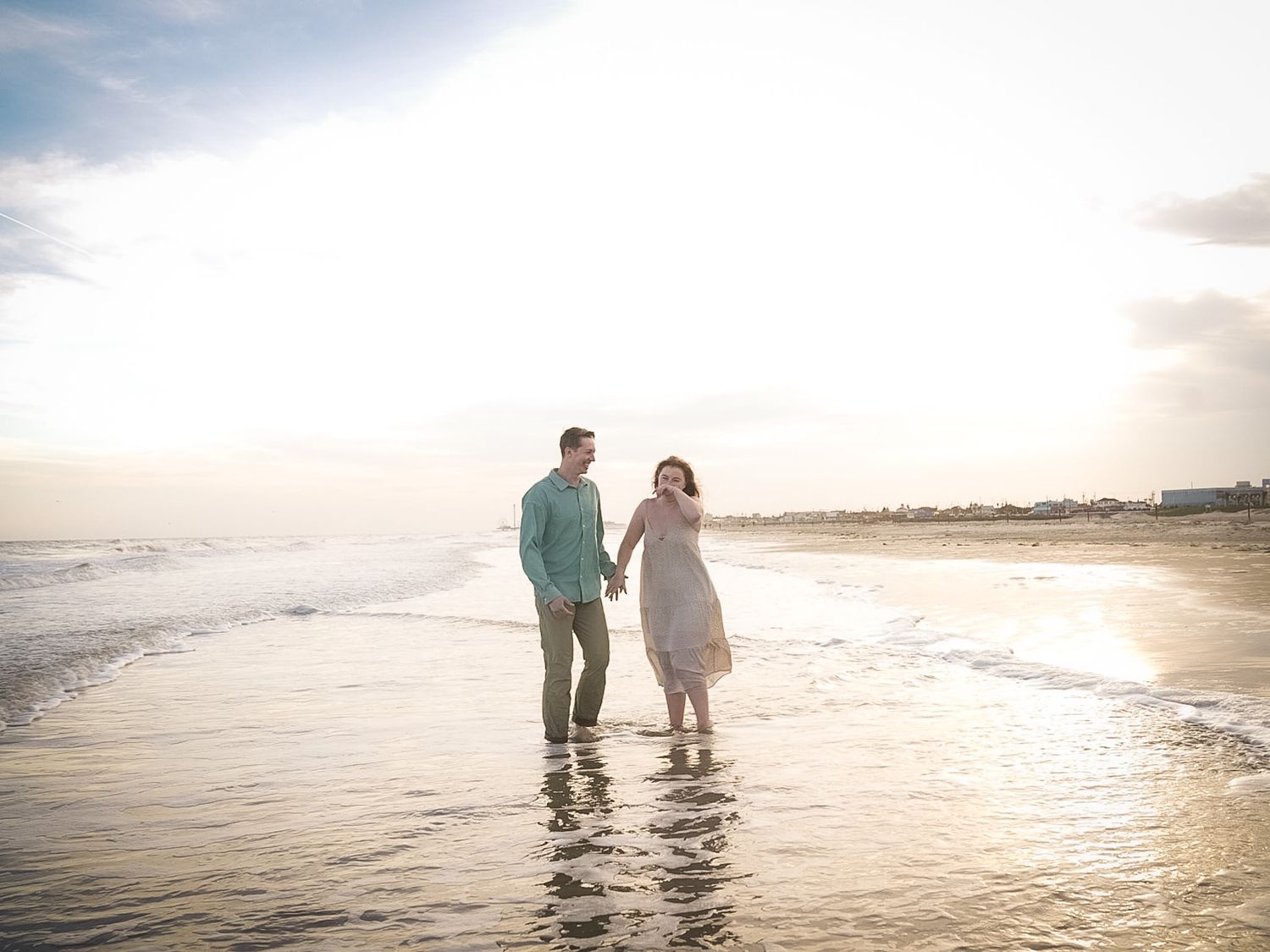 Couple walking hand in hand along a sunlit beach shoreline with gentle waves at golden hour.