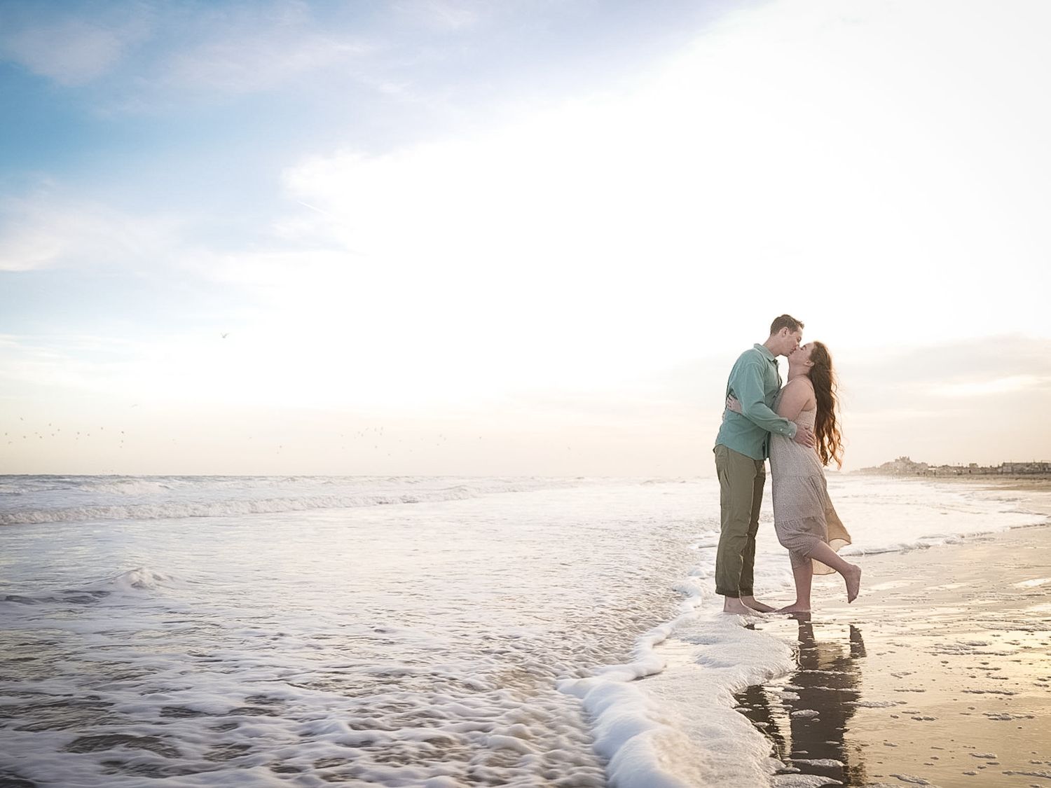 A couple shares a romantic kiss on the beach at golden hour sunset.