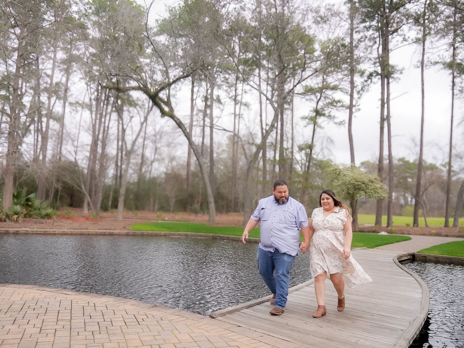 A couple walks hand in hand along a scenic pond path in the rain.