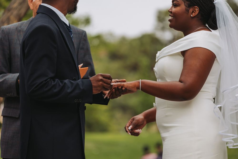 Bride and groom exchanging rings during an outdoor wedding ceremony, bride wearing white gown and veil.