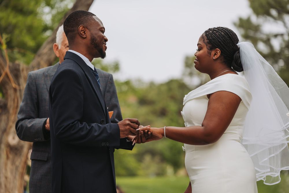 A couple exchanges wedding vows outdoors, with the groom in a suit and bride in a white dress and veil.