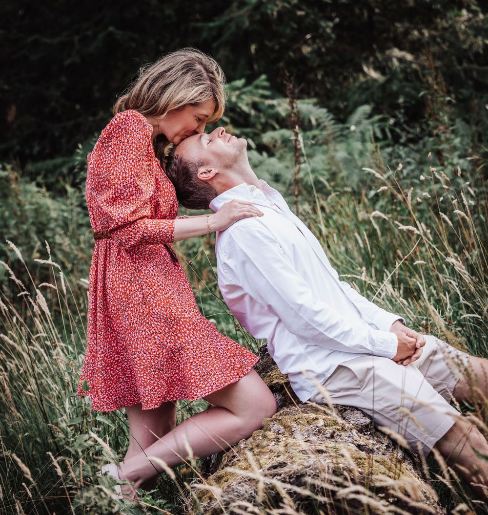 Romantic couple sharing a tender kiss in a lush green meadow, woman in red dress and man in white shirt.