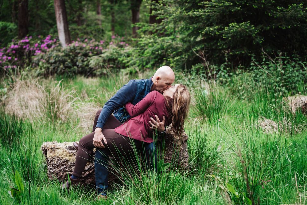 Couple sharing a romantic kiss on a log in a lush green garden setting.