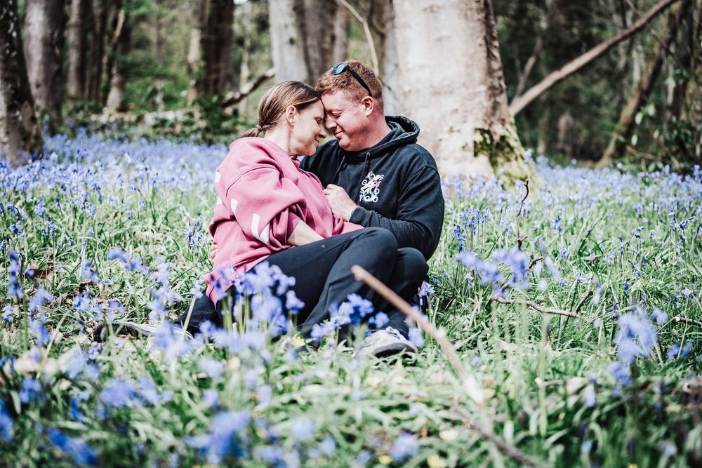 Couple sitting together in a bluebell woodland, sharing a romantic moment surrounded by spring wildflowers.