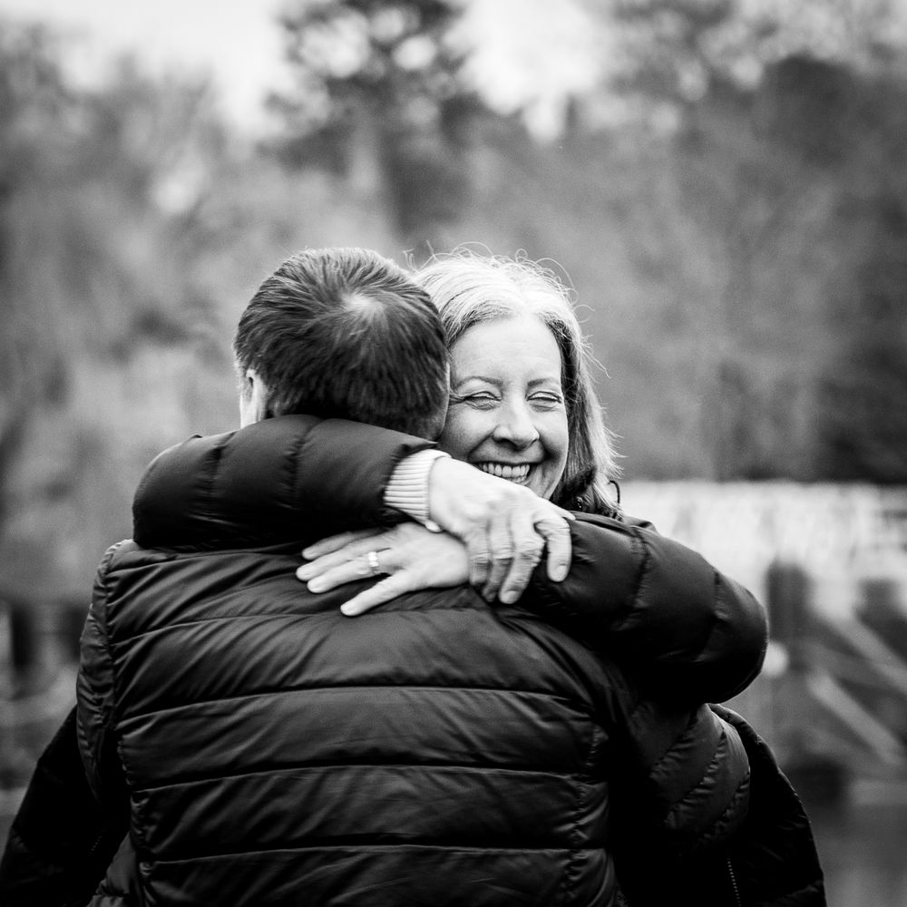 Black and white photo of a smiling woman hugging a man outdoors, capturing a warm and joyful embrace.