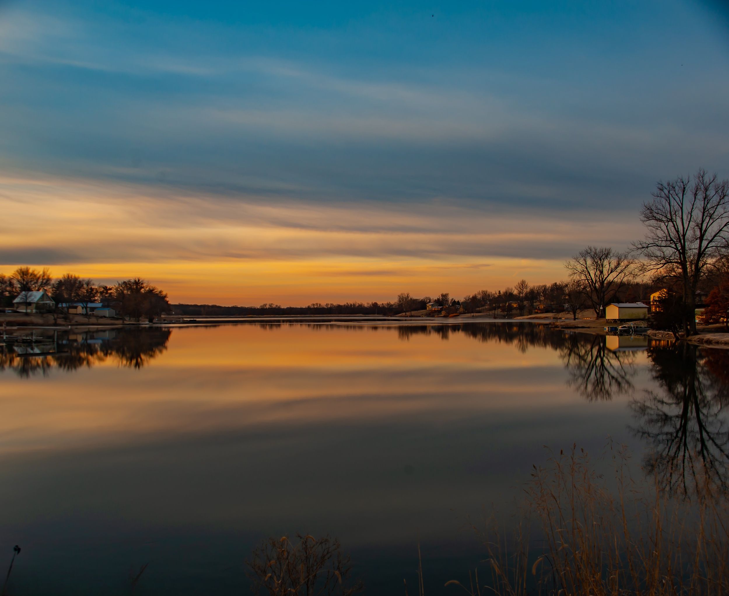 Mirror calm lake reflecting sunrise sky with bare trees and lake houses Northern Missouri