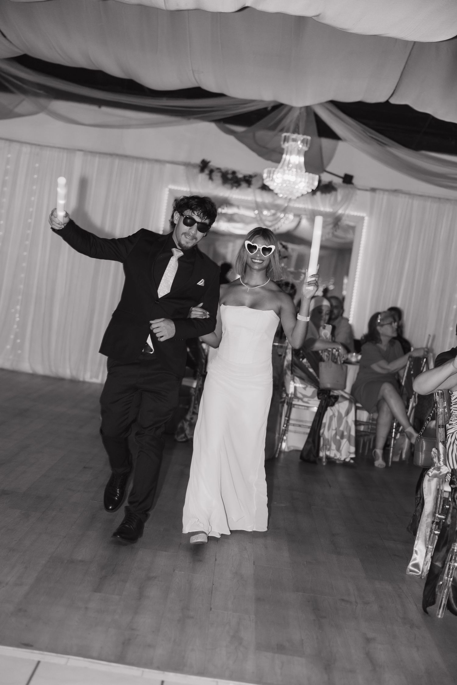 Black and white photo of bride and groom dancing with novelty sunglasses at wedding reception.
