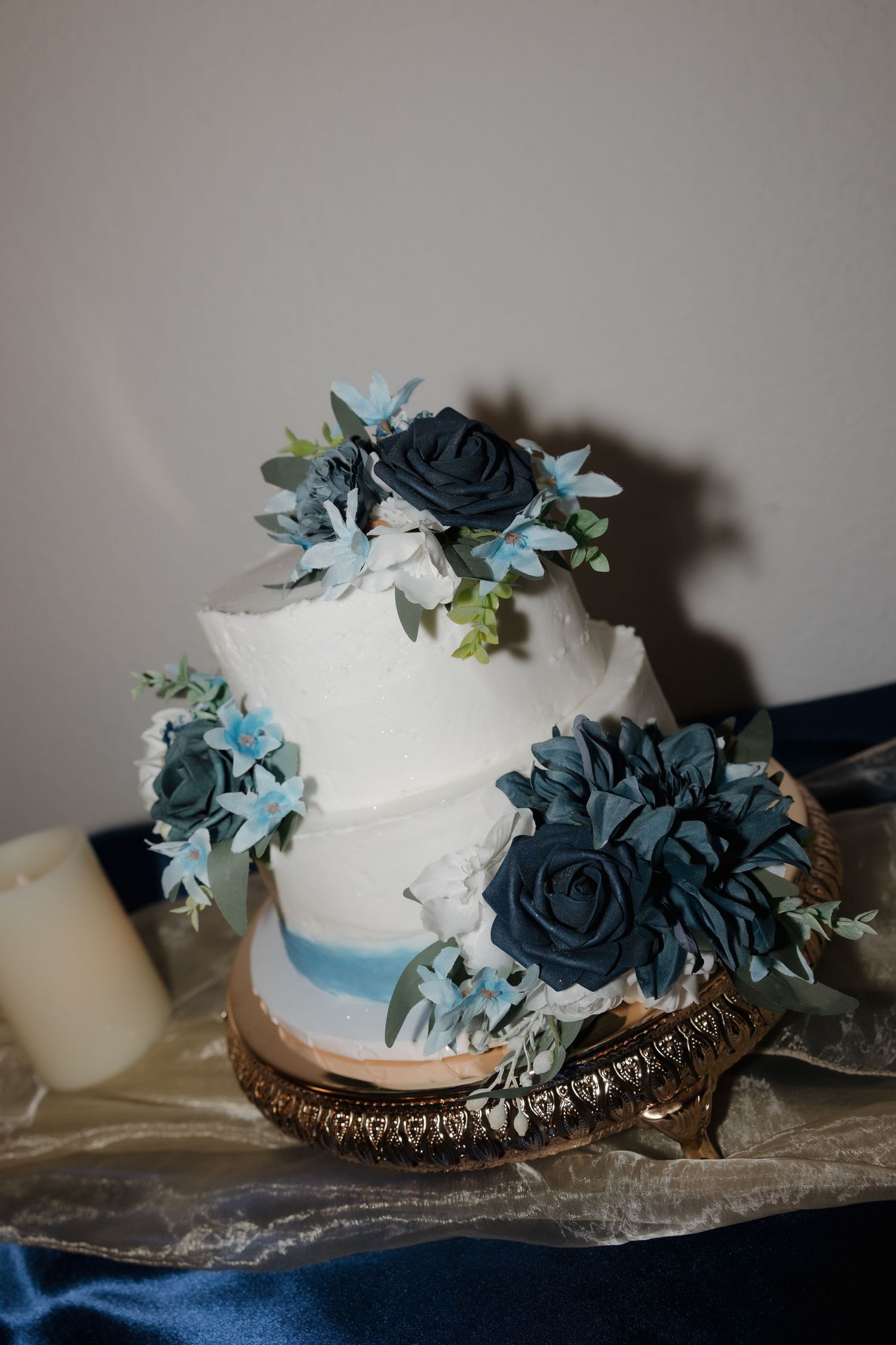 Two-tier white wedding cake with navy blue floral decorations on a rustic wooden stand.