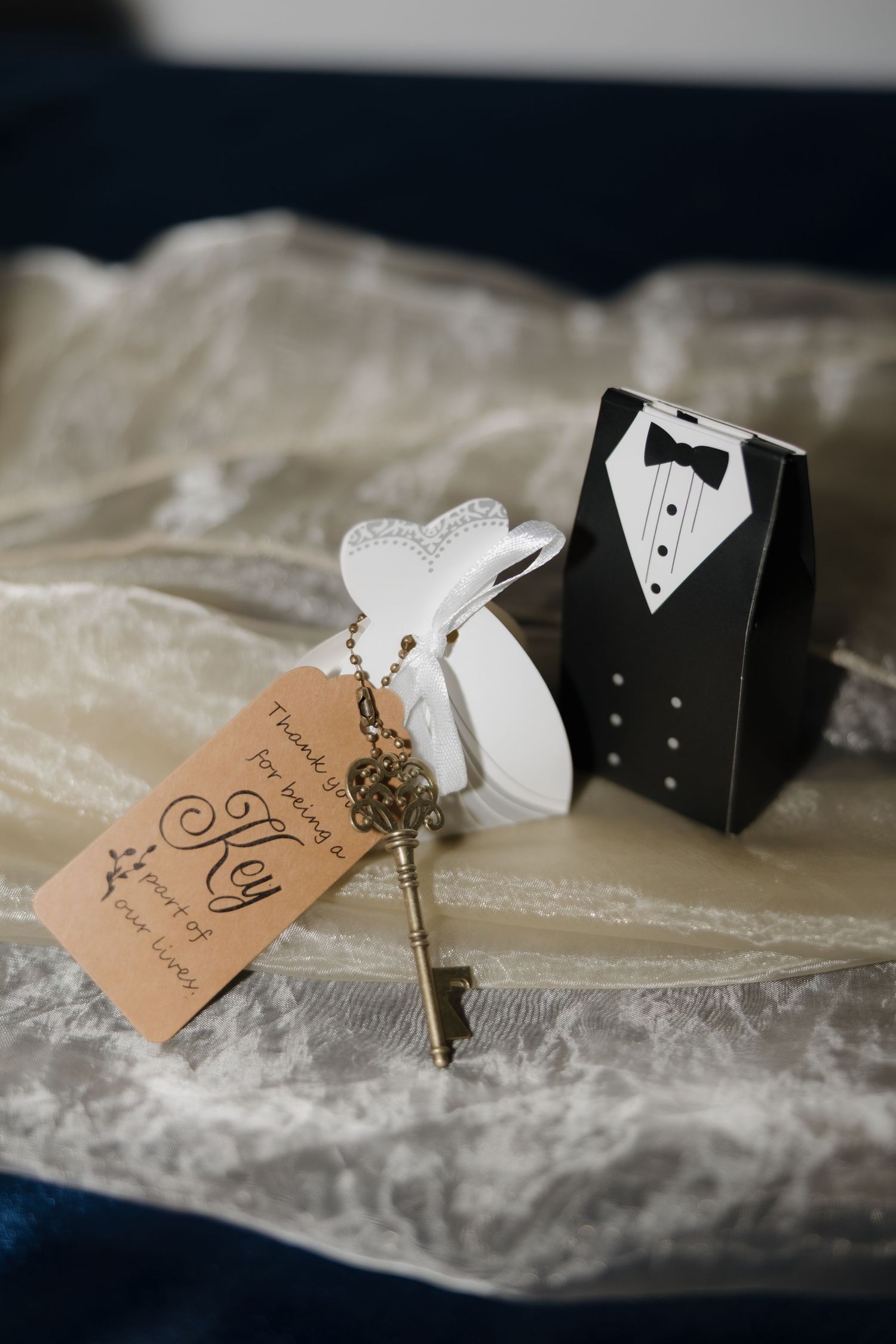 Wedding favor with vintage key, kraft tag, and bride and groom gift boxes on lace fabric.