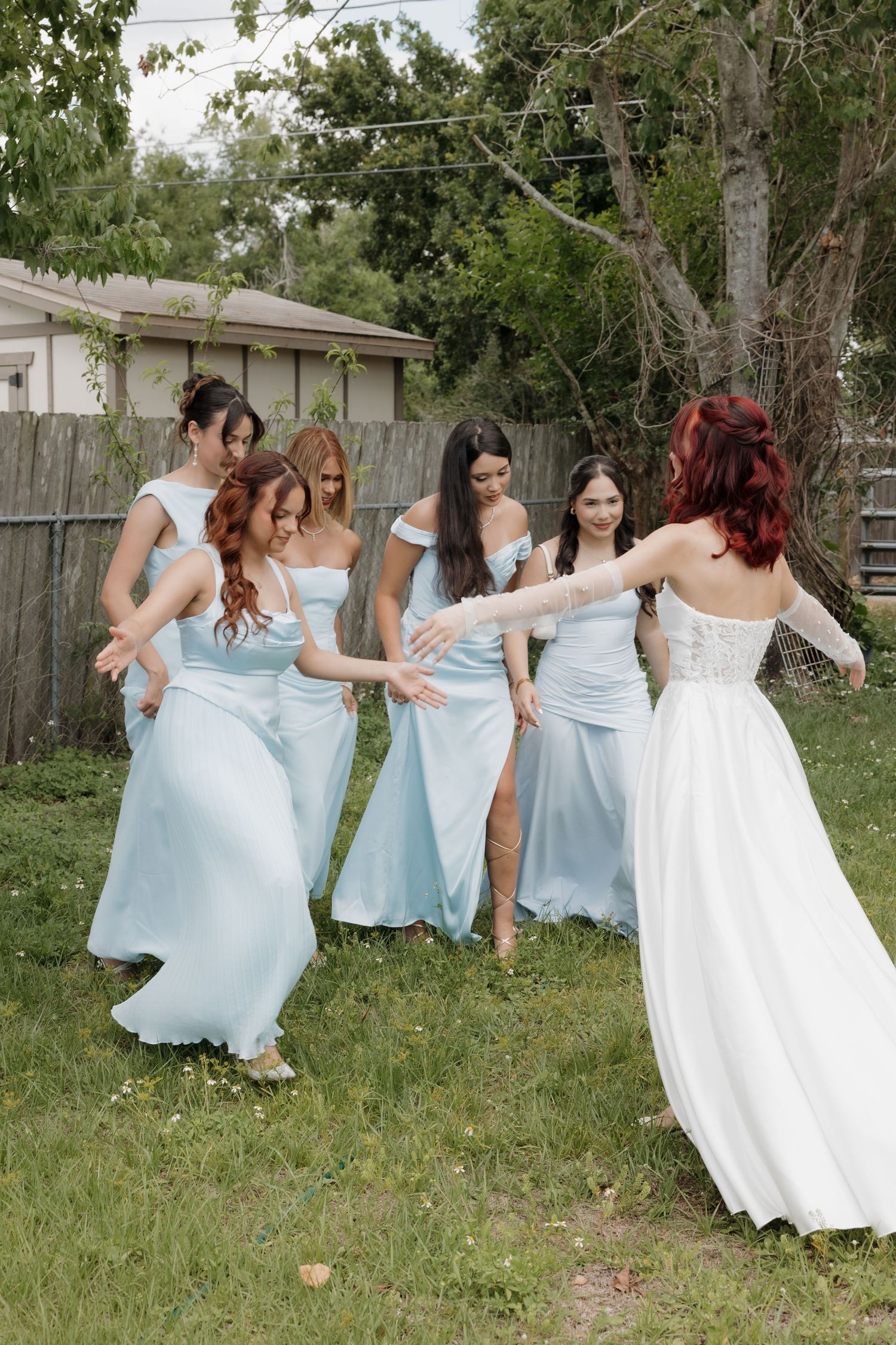 Bride in white gown with bridesmaids in light blue dresses celebrating outdoors on wedding day.