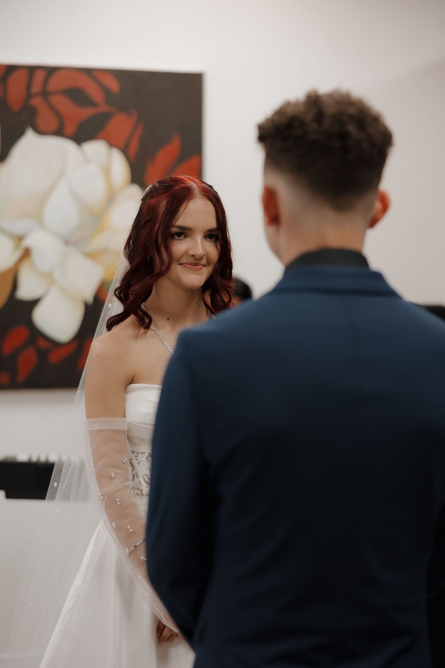 Bride in white strapless gown smiling at groom in navy suit during wedding ceremony.
