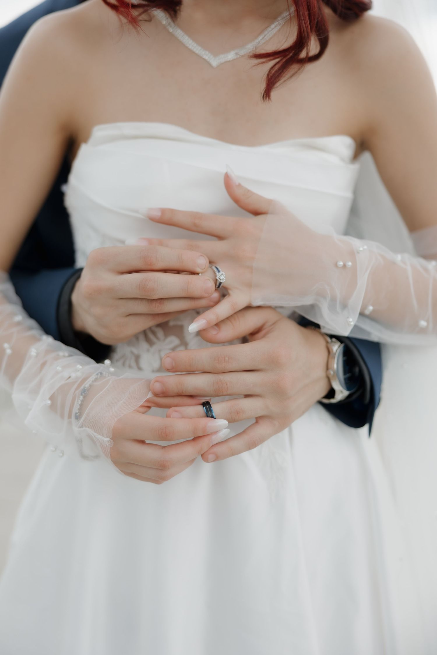 Bride and groom showing off their wedding rings, hands intertwined, wearing elegant wedding attire.