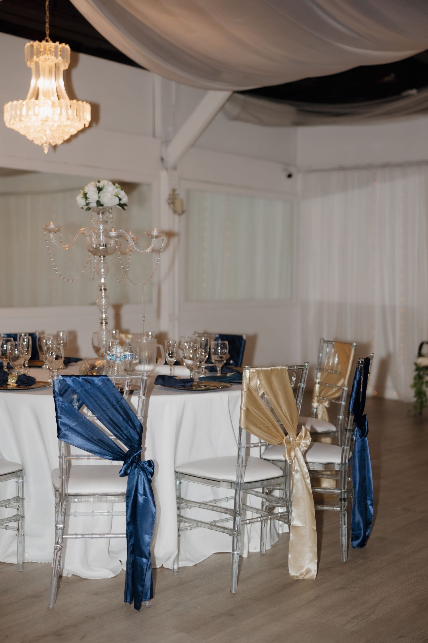 Elegant wedding reception table with navy and gold chair sashes and crystal chandelier.