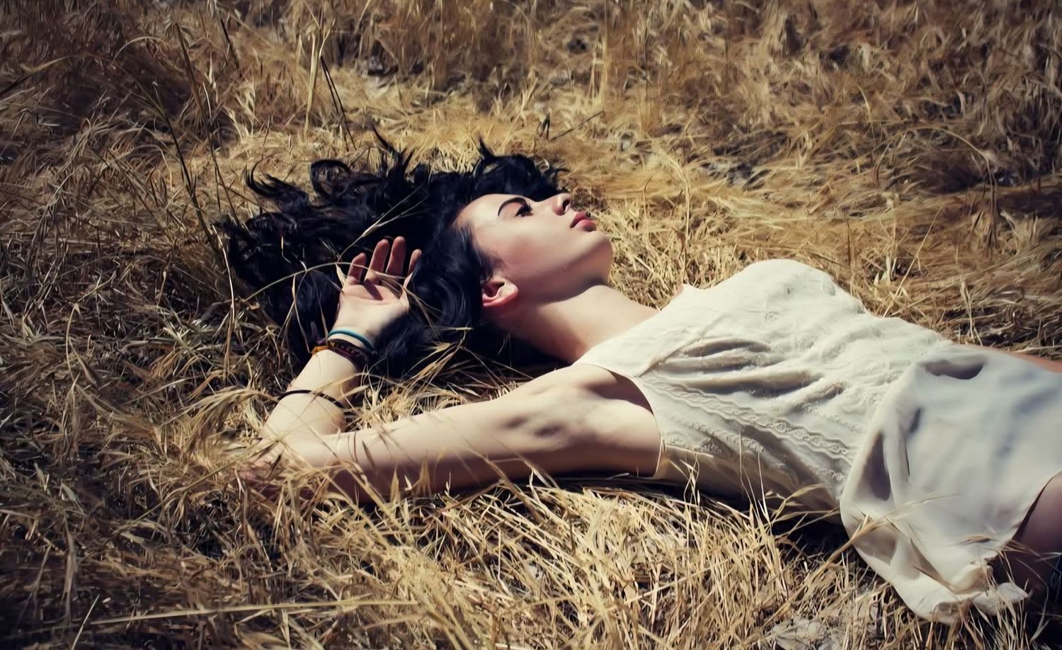 A young woman laying down in a dry grass field.