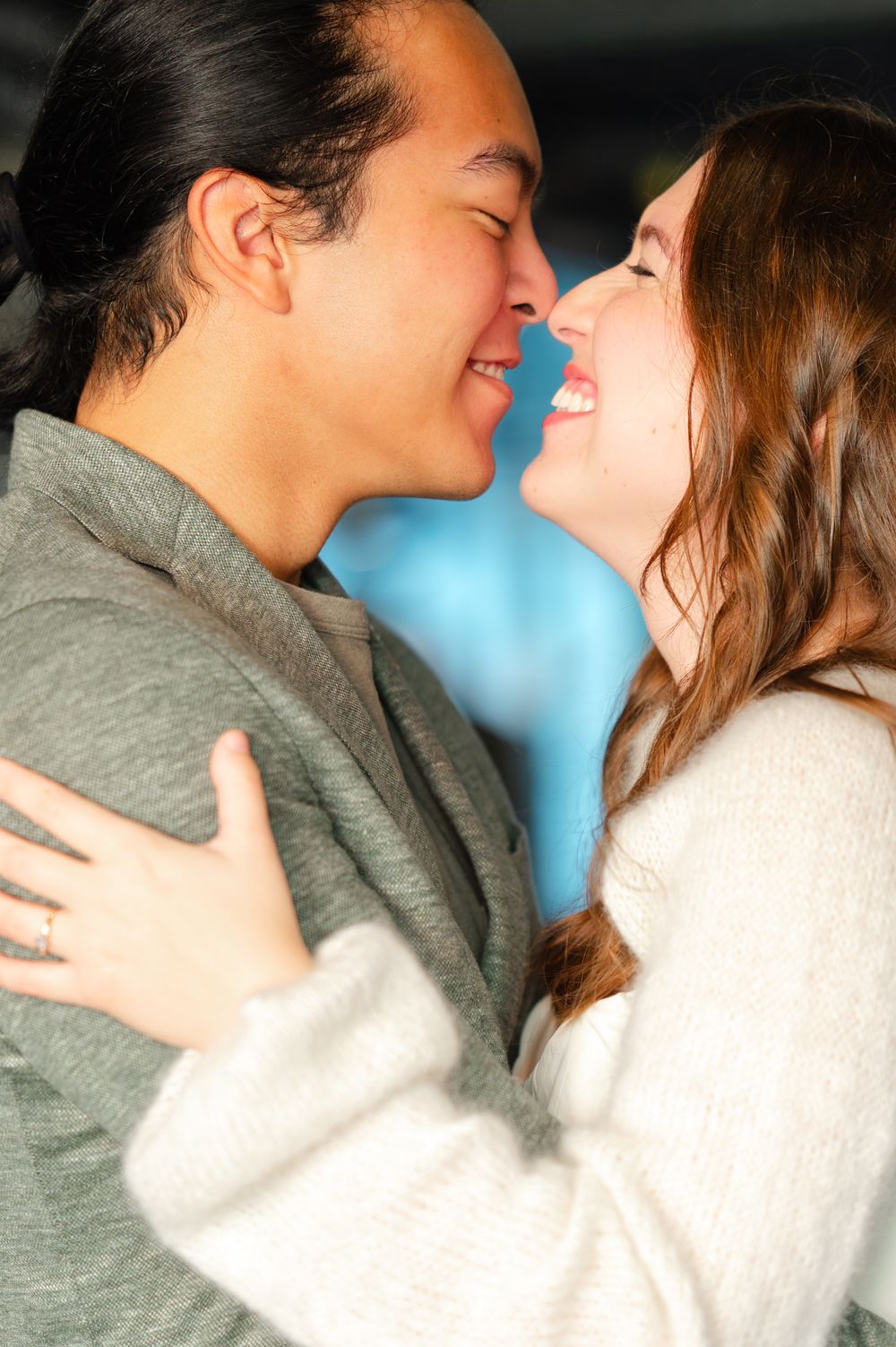 Happy couple embracing and smiling face to face, woman in white sweater, man in gray jacket, sharing a joyful moment.