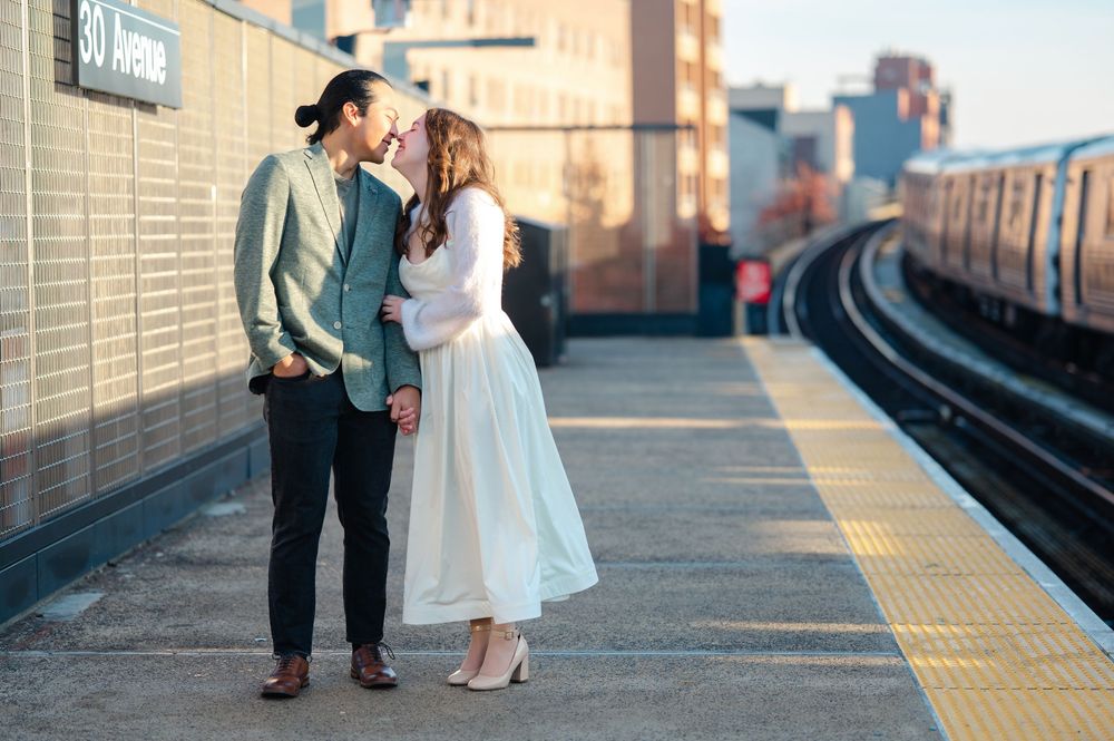 Couple sharing a tender moment on 30 Avenue subway platform, woman in white dress and man in teal shirt.
