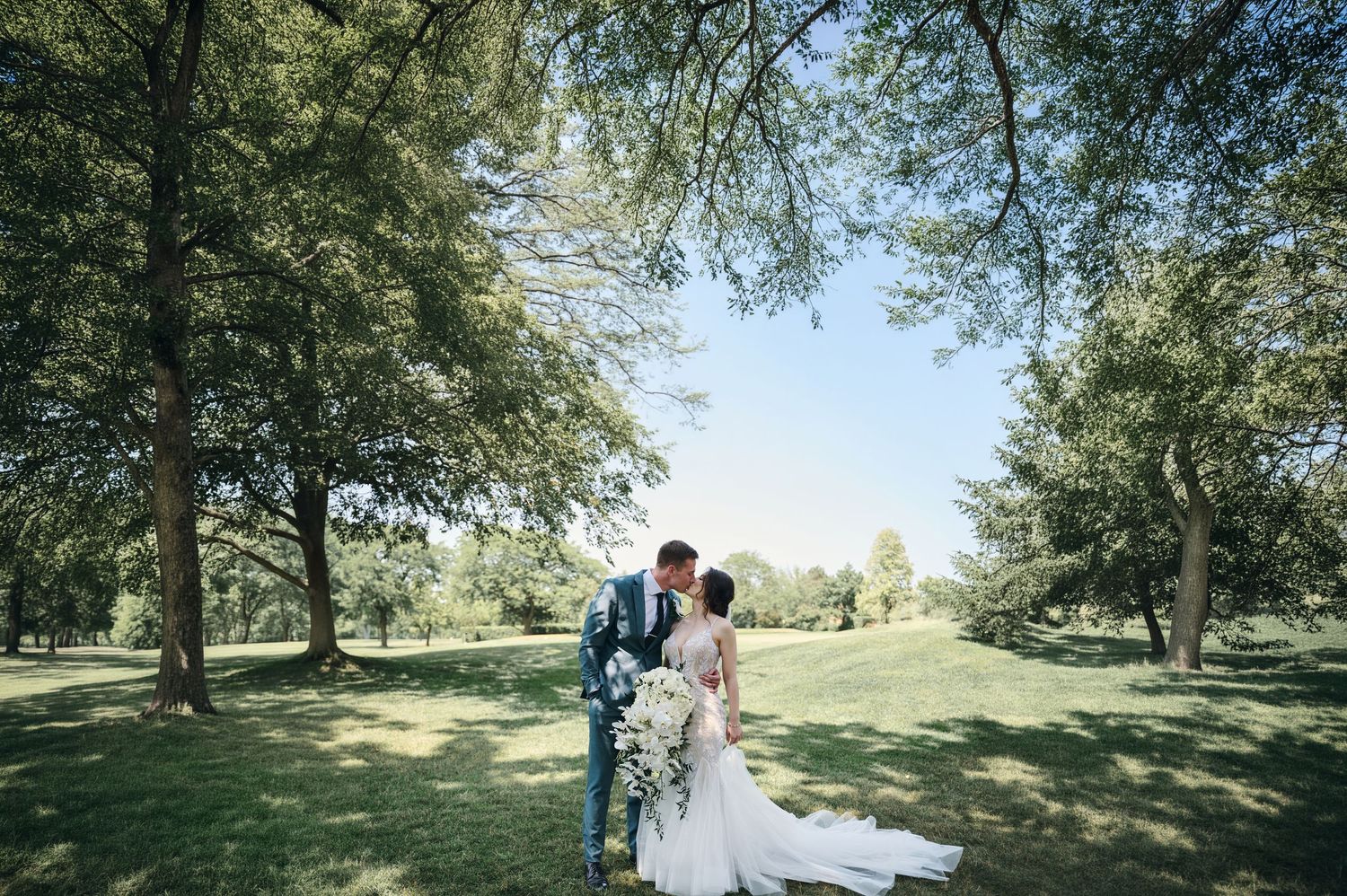 Bride in a strapless ball gown with ruffled skirt and veil sits on a navy sofa before a brick wall.