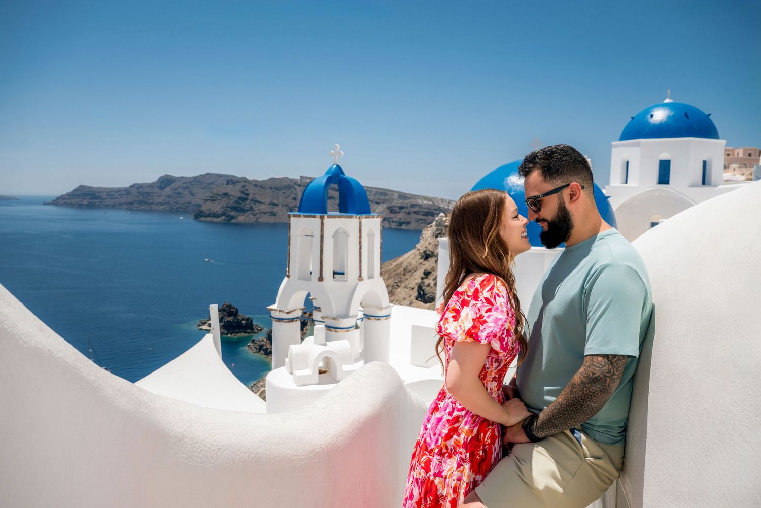 Romantic couple embracing in Santorini, Greece, with iconic blue-domed churches and Aegean Sea views.
