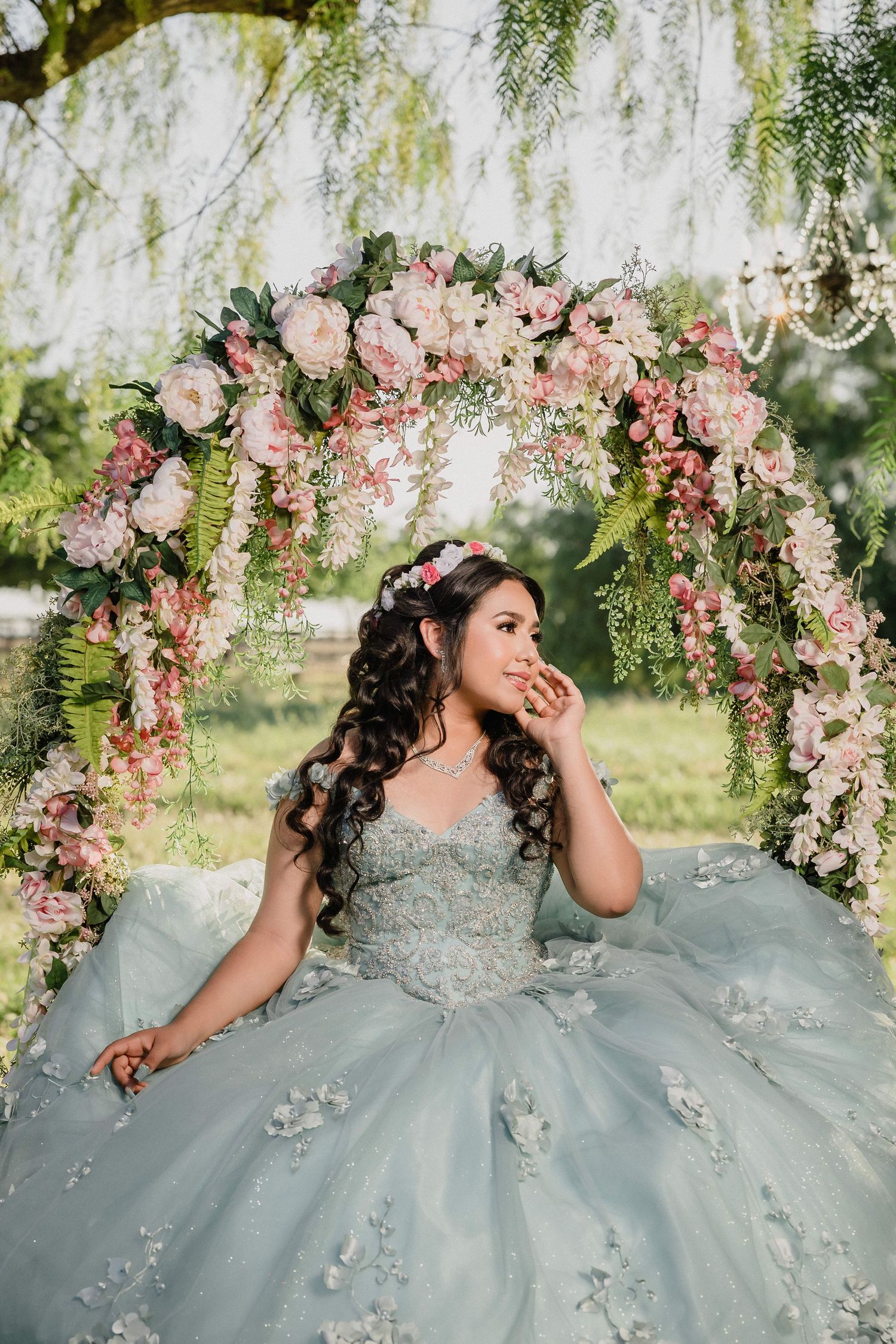 Woman in blue ballgown on ornate gold staircase in elegant mansion with arched windows and chandelier.