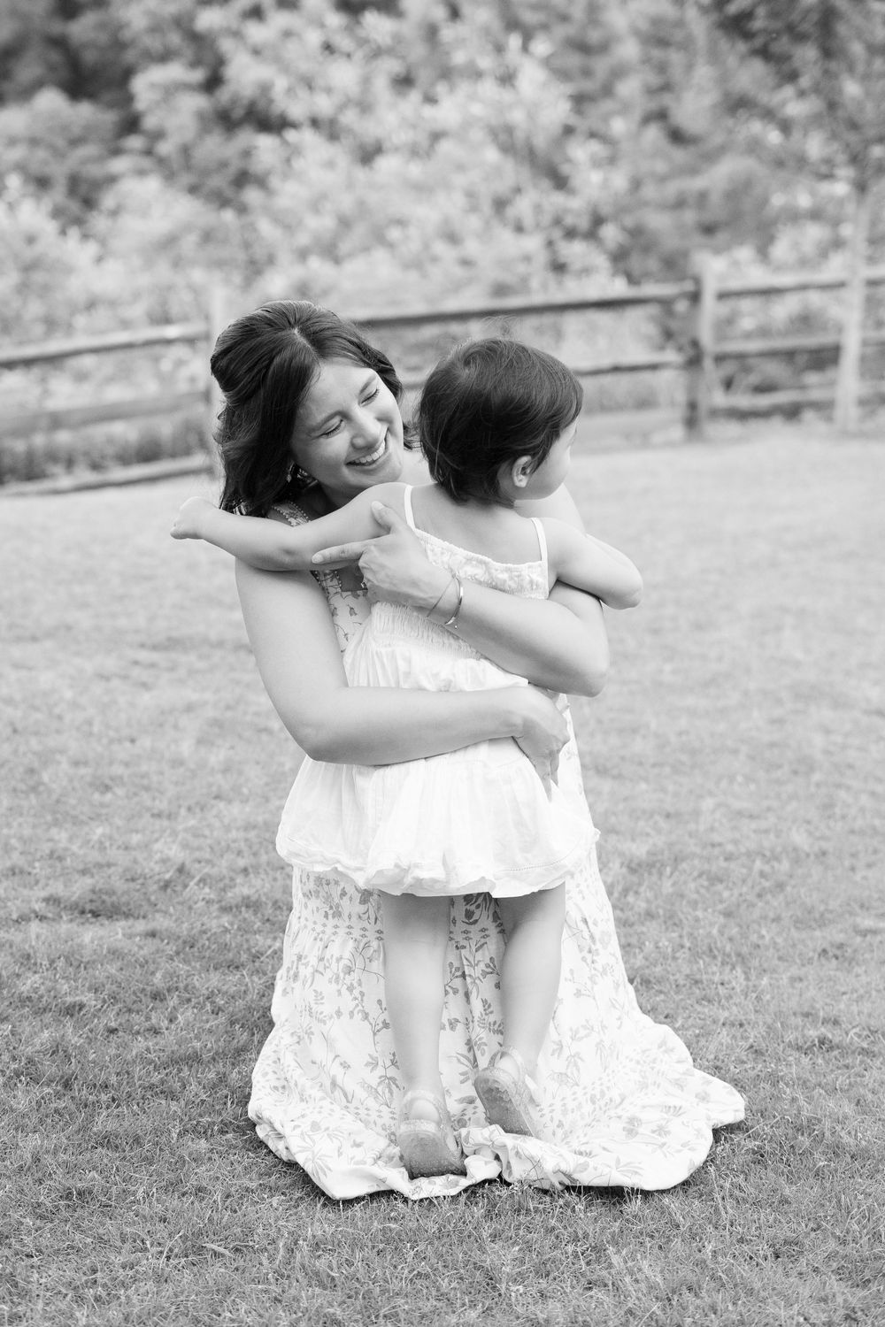 Black and white photo of a joyful mother holding and smiling at her baby on a green lawn.