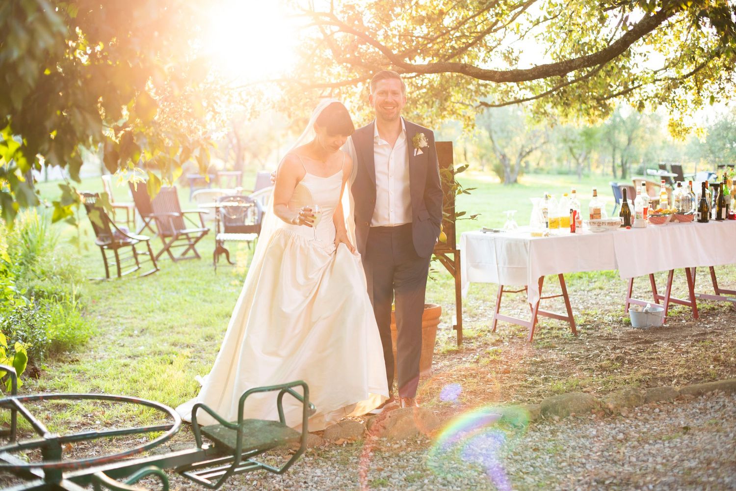 Bride and groom walking together in sunlit garden at outdoor wedding reception venue.