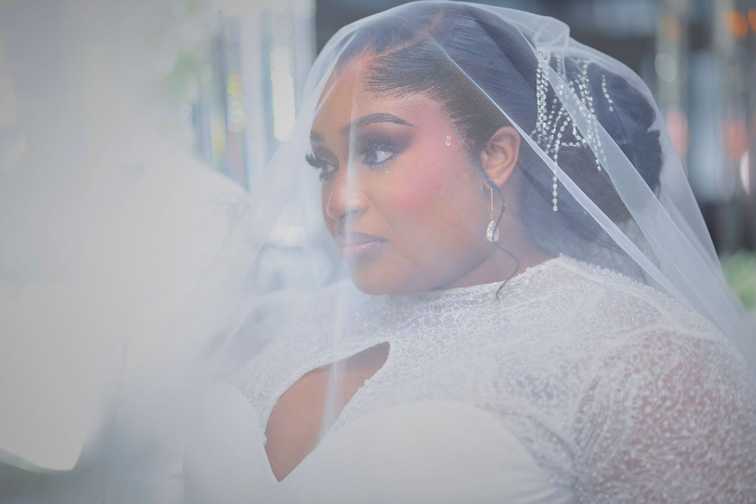 A bride wearing a beaded white gown and flowing veil with crystal hair accessories on her wedding day.