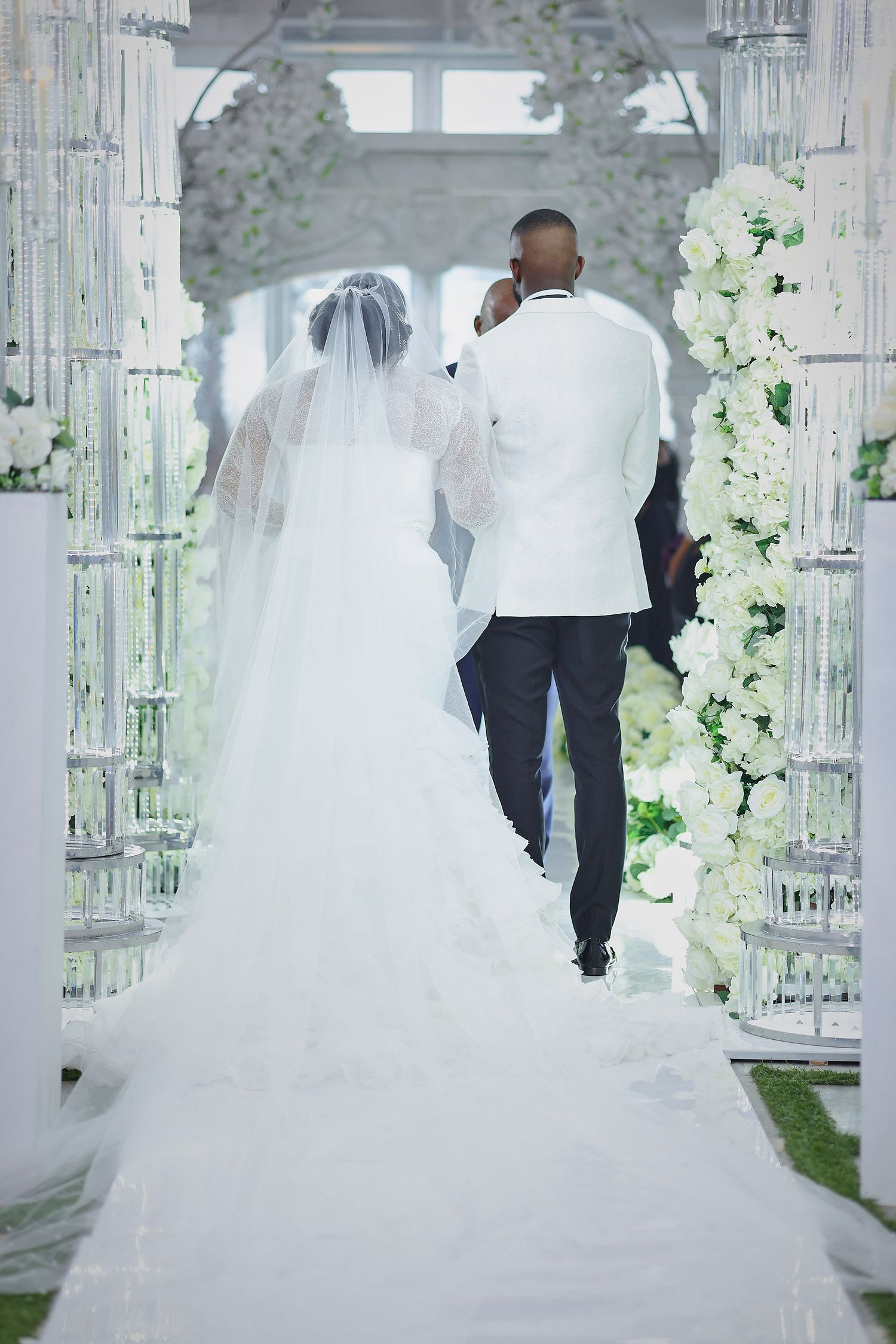 A bride and groom walk away down a white floral aisle during their elegant wedding ceremony.