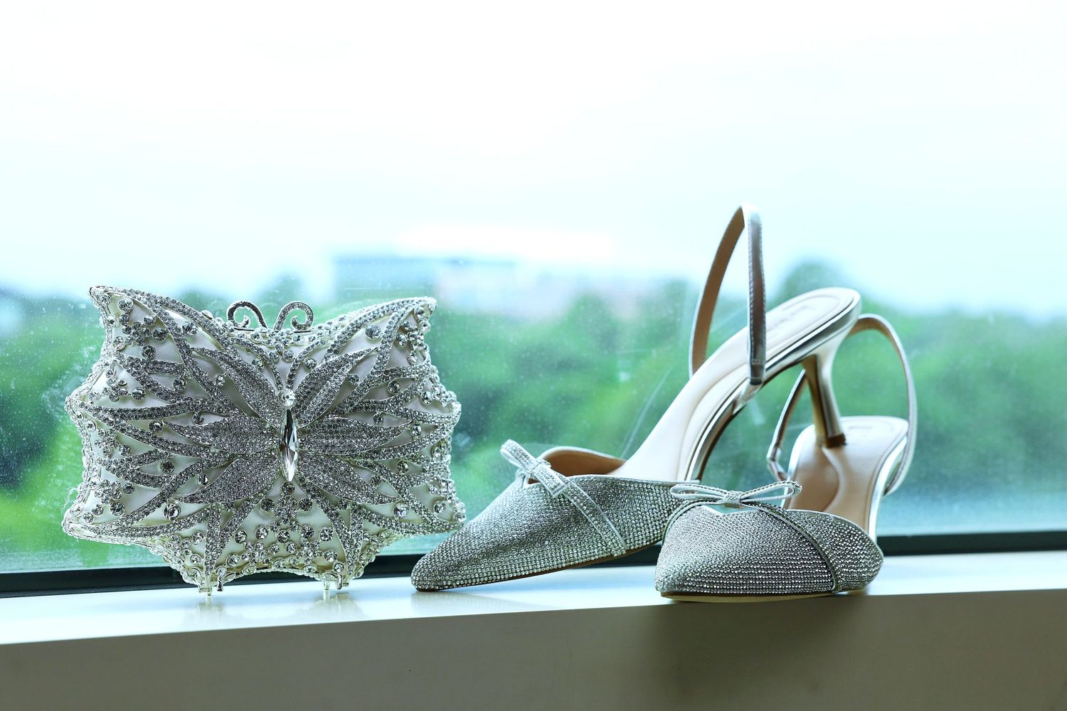 Elegant silver glitter heels and butterfly clutch purse displayed on a windowsill for a wedding.