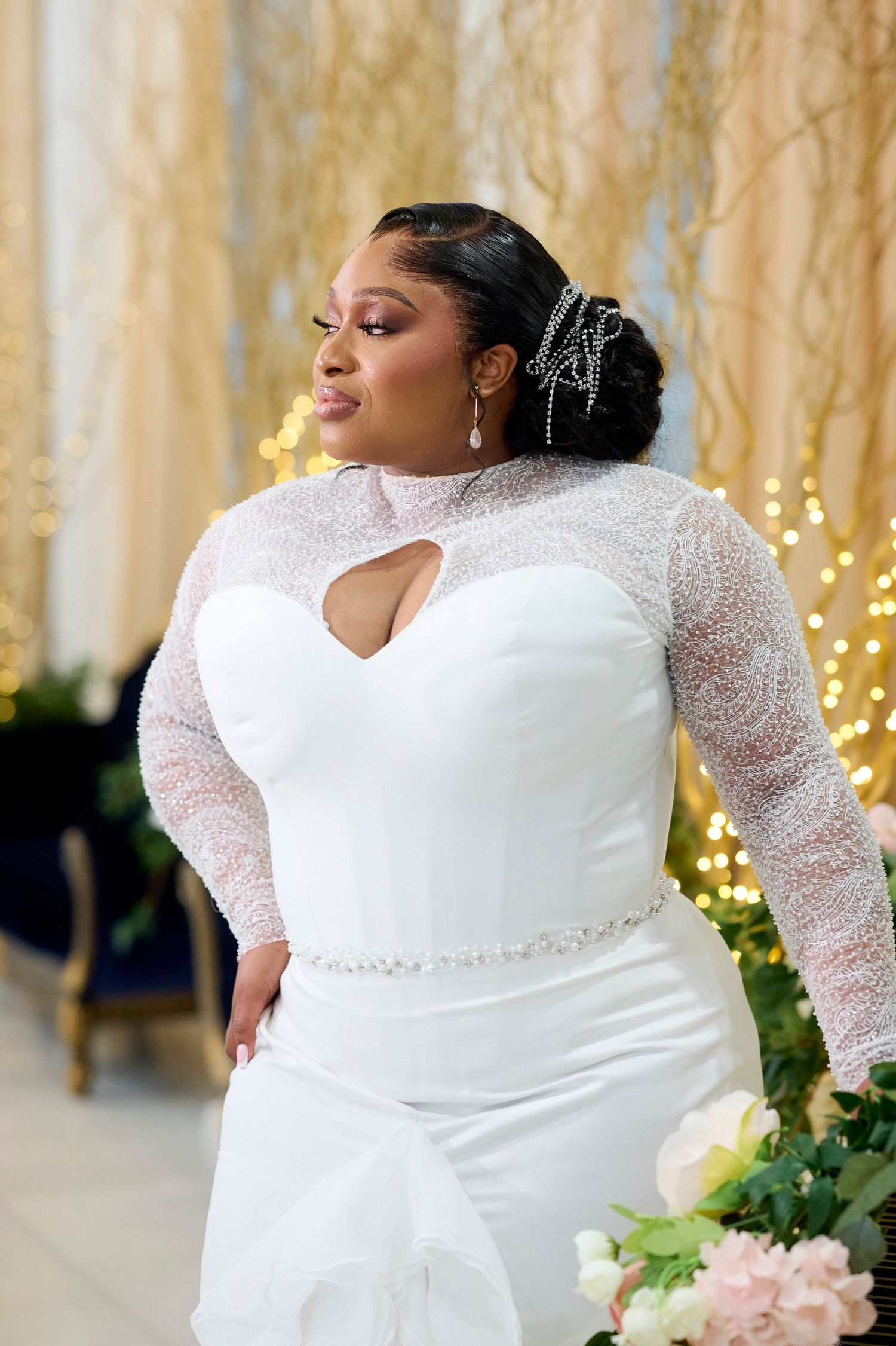 Plus-size bride in white mermaid gown with beaded long sleeves and keyhole neckline, adorned with pearl hair accessories.