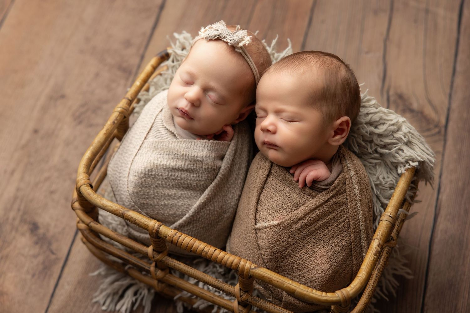 Sleeping newborn baby wrapped in teal swaddle inside a small bucket with a green pillow.