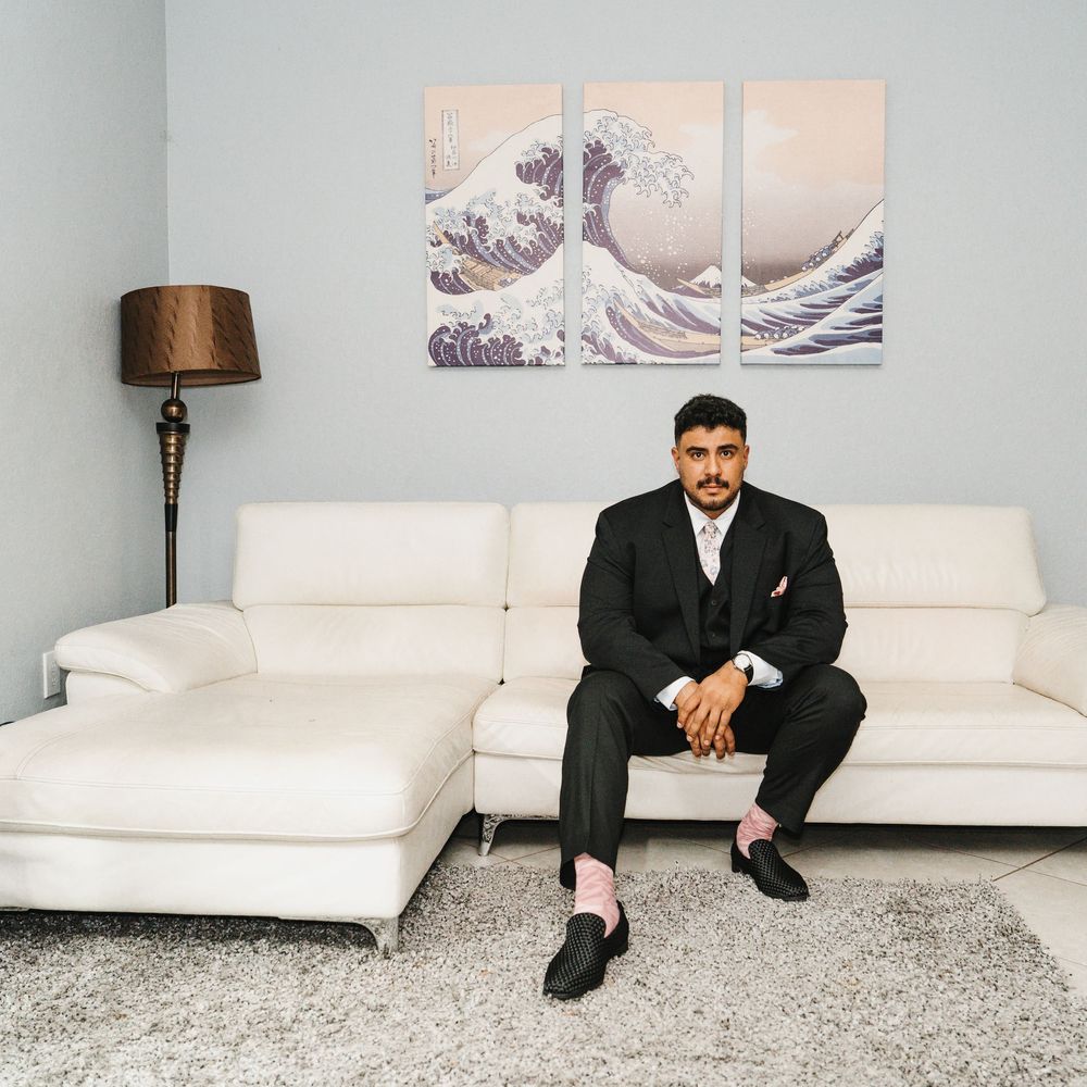 Man in black suit sitting on white sofa with Hokusai Great Wave triptych wall art in modern living room.