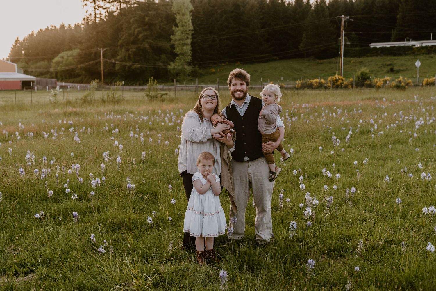 Family of five posing in a wildflower meadow at golden hour, surrounded by lush green grass and trees.