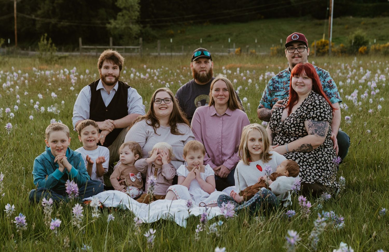 Large family portrait in a wildflower meadow, adults and children smiling together outdoors.