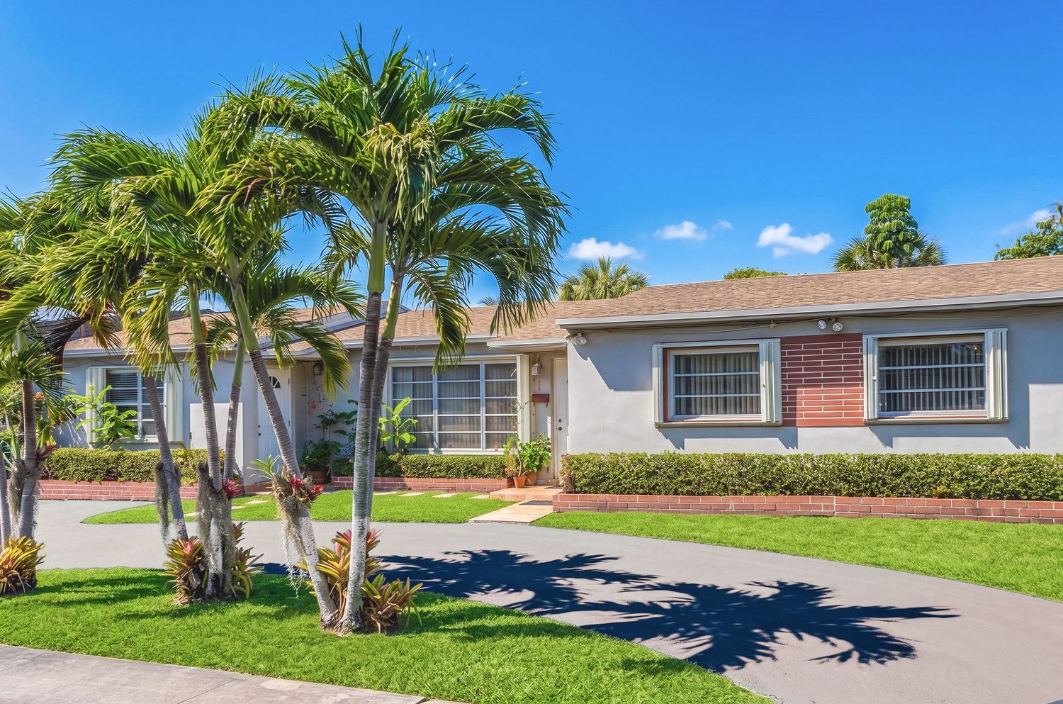 Single-story Florida home with palm trees, brick accents, blue-gray exterior, and lush green lawn on a sunny day.