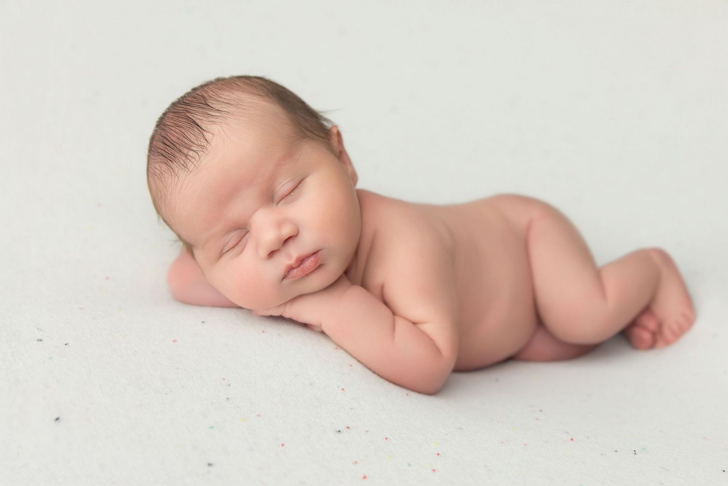 Newborn baby wrapped in teal swaddle holding green knit bear toy, resting in decorative bucket.