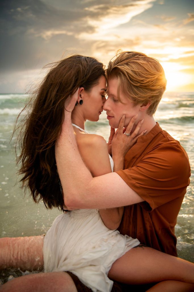 Intimate couples engagement session at sunset with a couple embracing in the waves on a Florida beach. Golden sun lighting their hair.