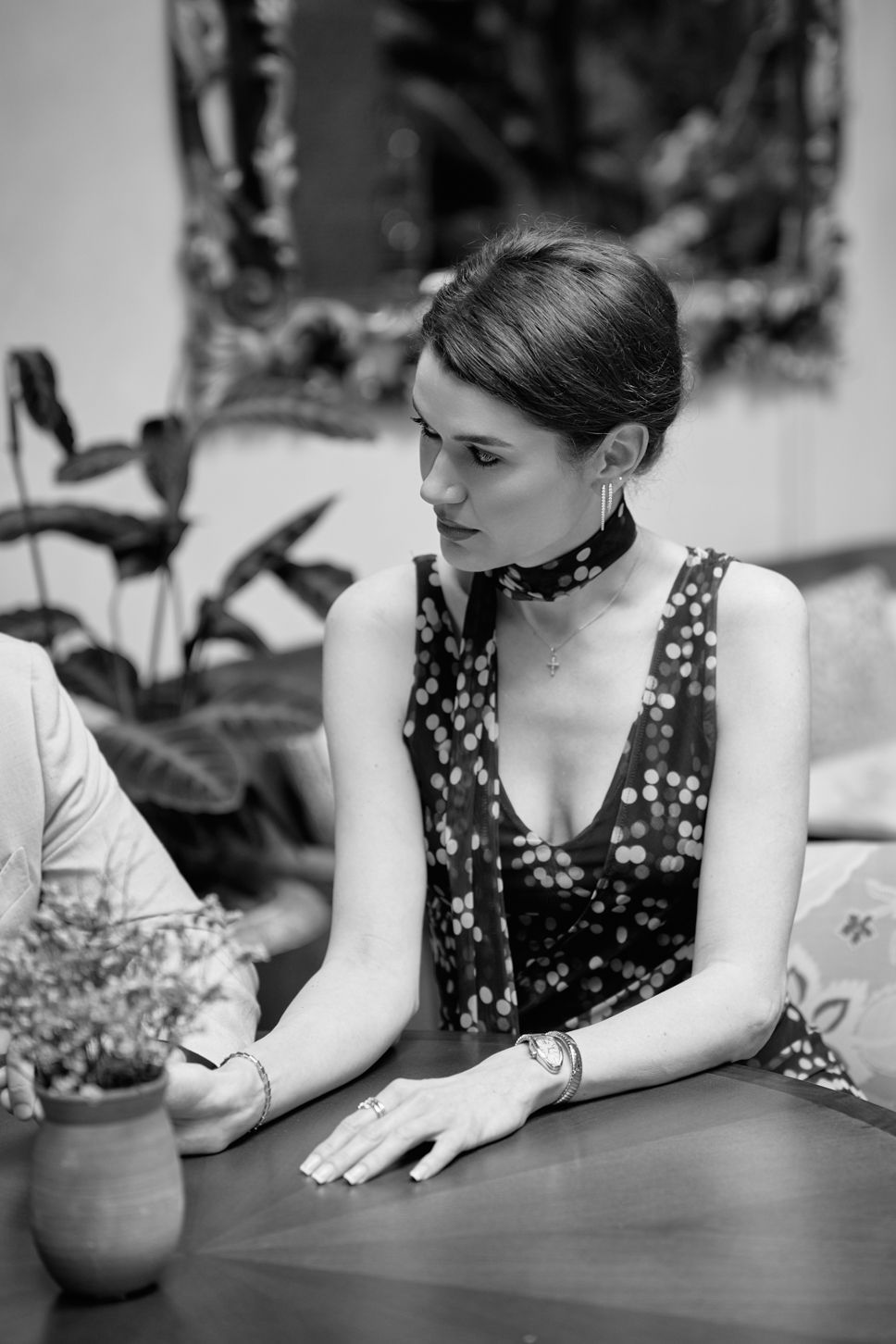 Black and white portrait of an elegant woman in a patterned dress with choker necklace seated at a table.