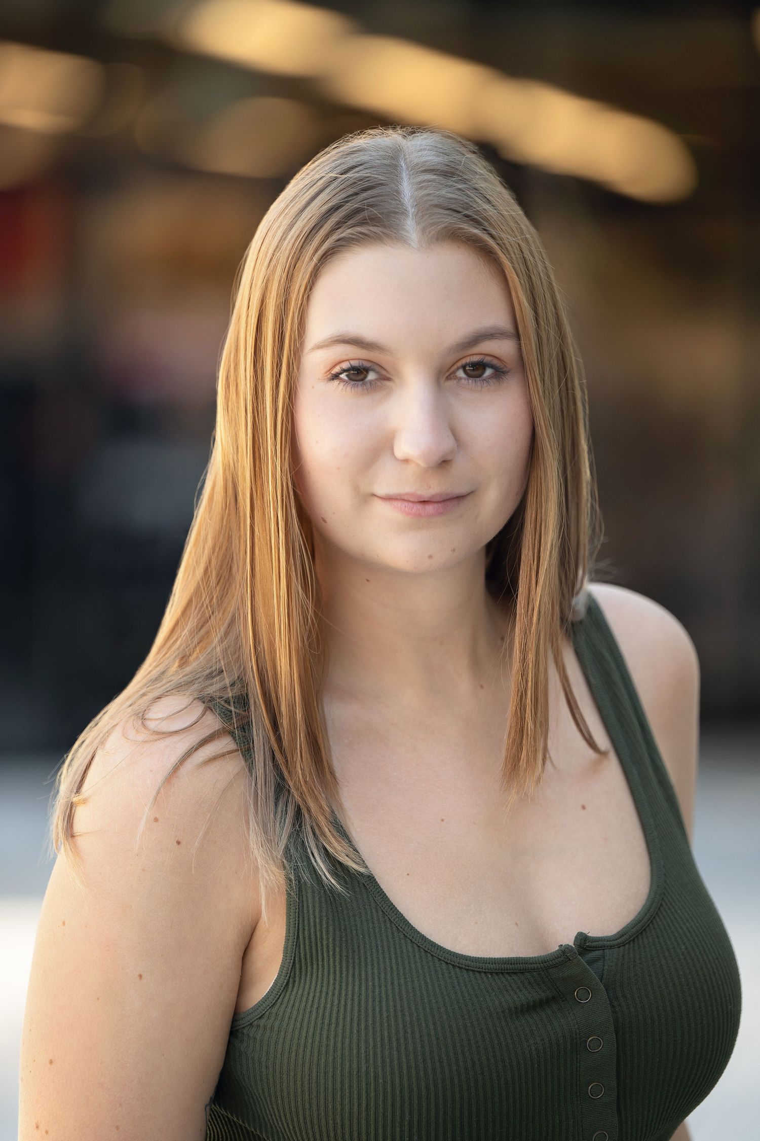Young blonde woman in olive tank top poses for a natural light portrait outdoors.