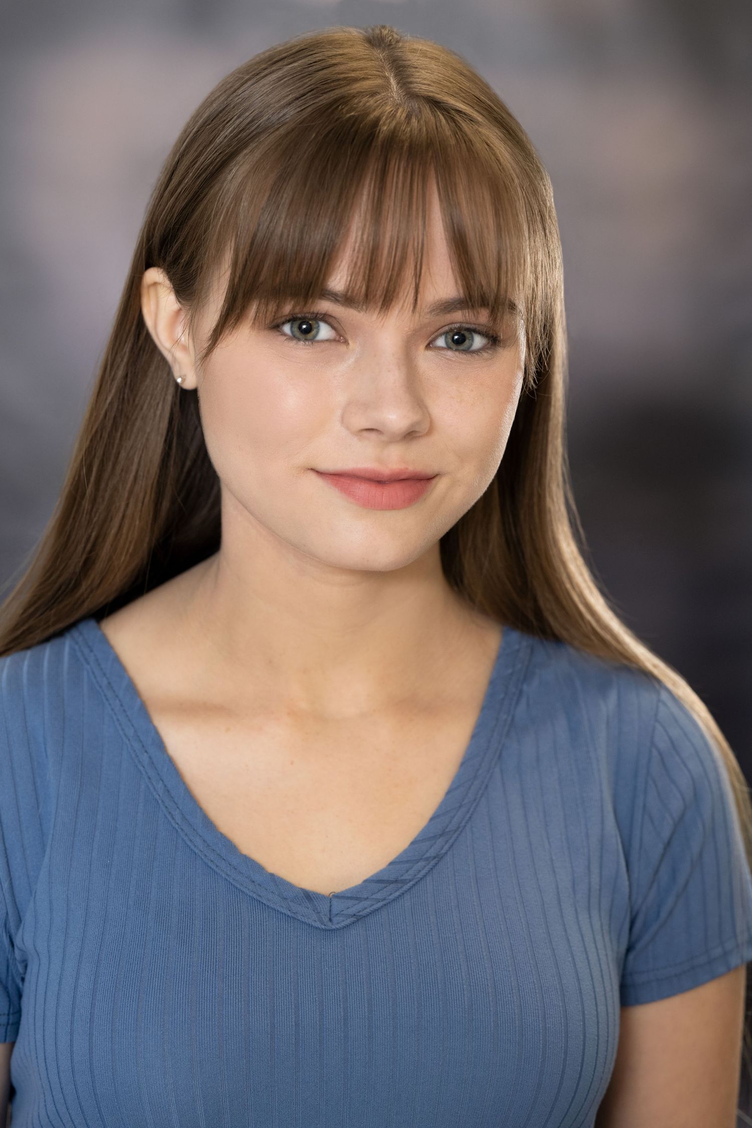 Young woman with long brown hair and bangs poses in a blue top for a headshot.