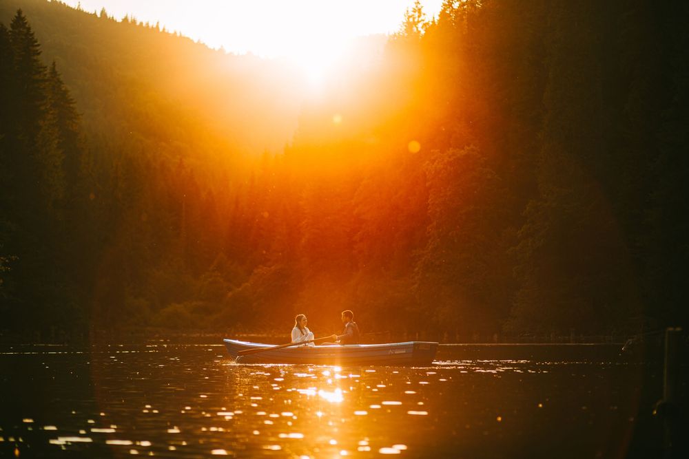 Two people kayaking on a serene lake surrounded by lush pine forests bathed in a stunning golden sunset glow.