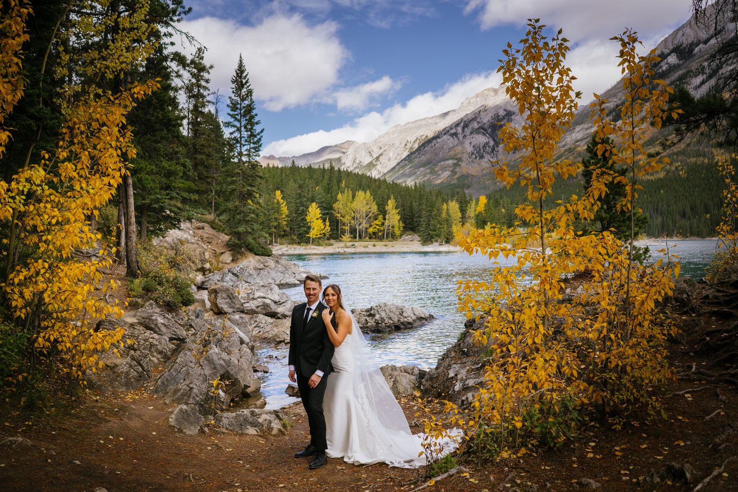 A scenic mountain wedding photo with fall foliage, a river, and peaks in the background.