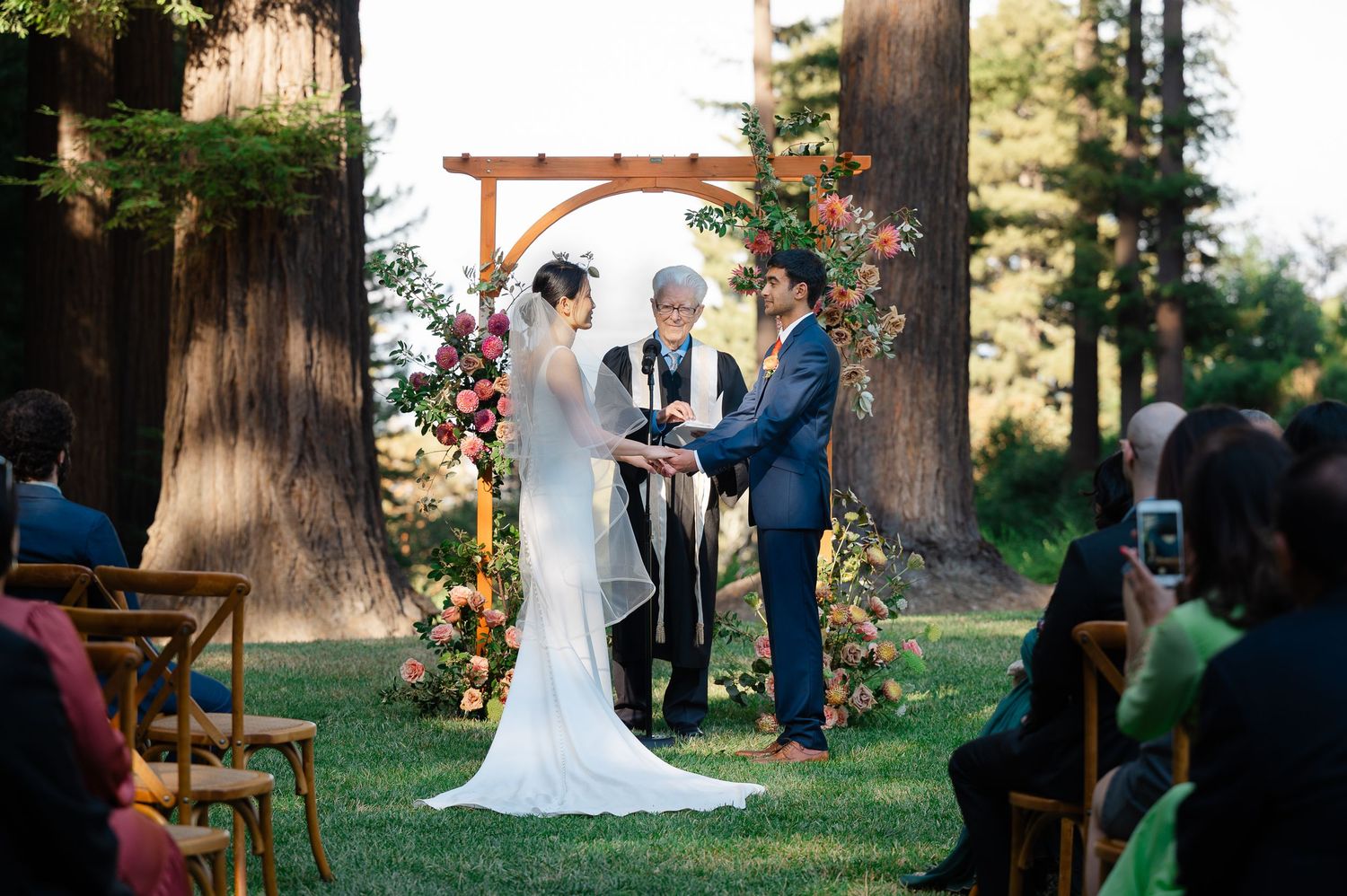 Bride and groom pose in front of cactus garden with golden mountain backdrop at outdoor wedding.