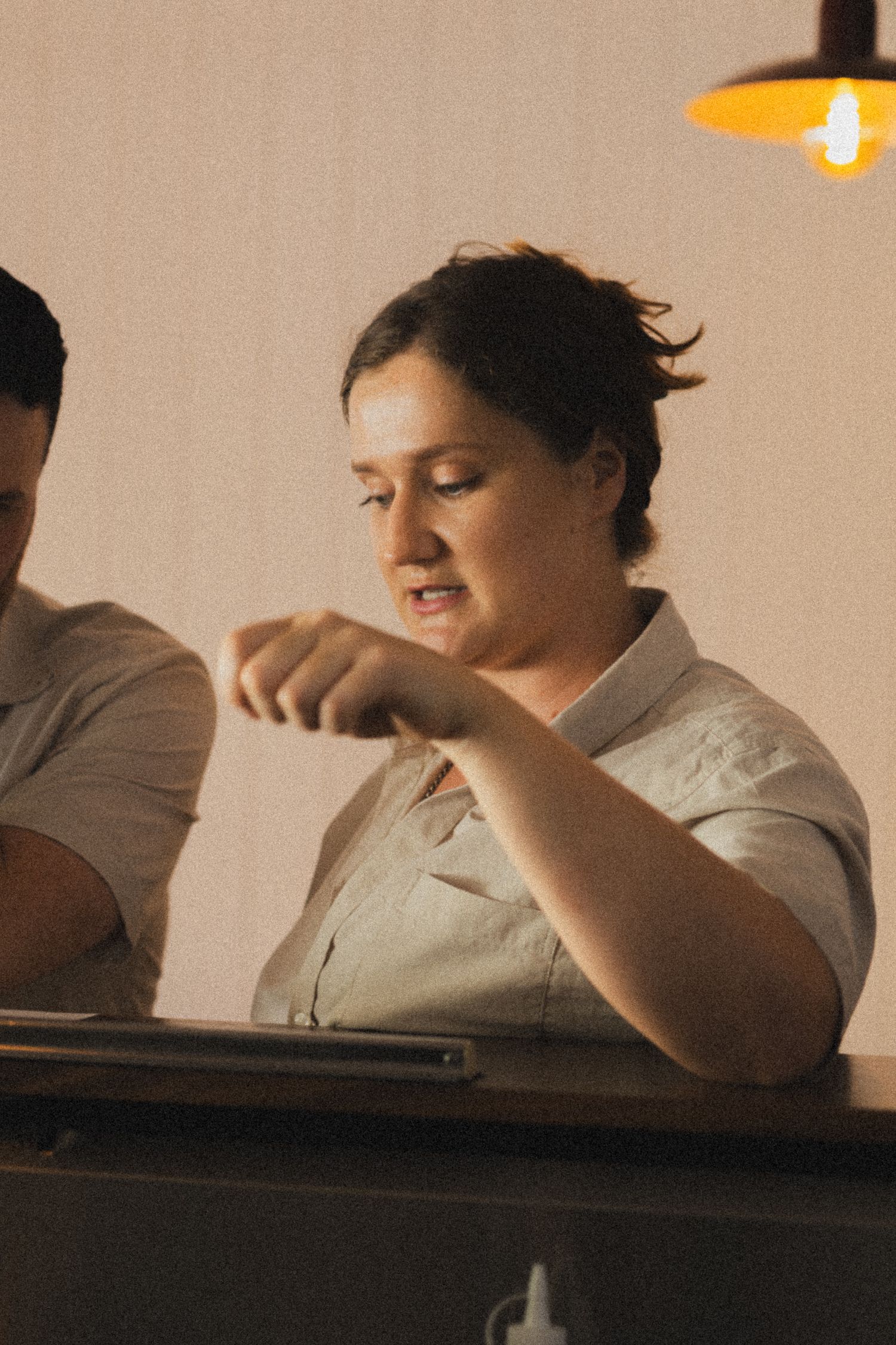 Woman in white shirt gesturing with hands at a desk under warm lighting in a casual indoor setting.